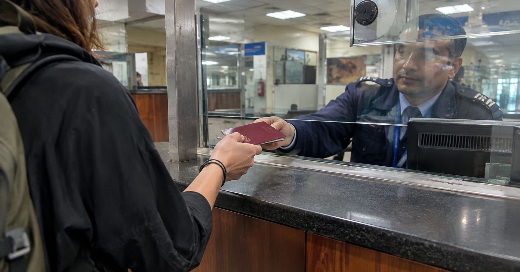 Traveler handing a passport to an immigration officer at a visa counter in Nepal